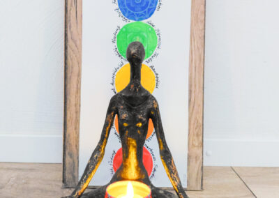 Holzfigur im Meditationssitz mit Kerze und Chakren-Symbolen
